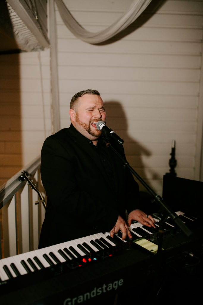 A man plays piano while singing at a wedding reception